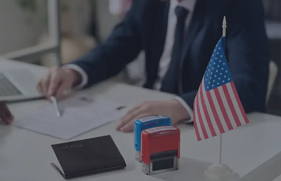 Oficina legal profesional con una mujer de saco sentada en un escritorio con documentos legales, un mazo y una estatua de la justicia. El texto superpuesto dice “¿Por qué contratar a un abogado de inmigración?”