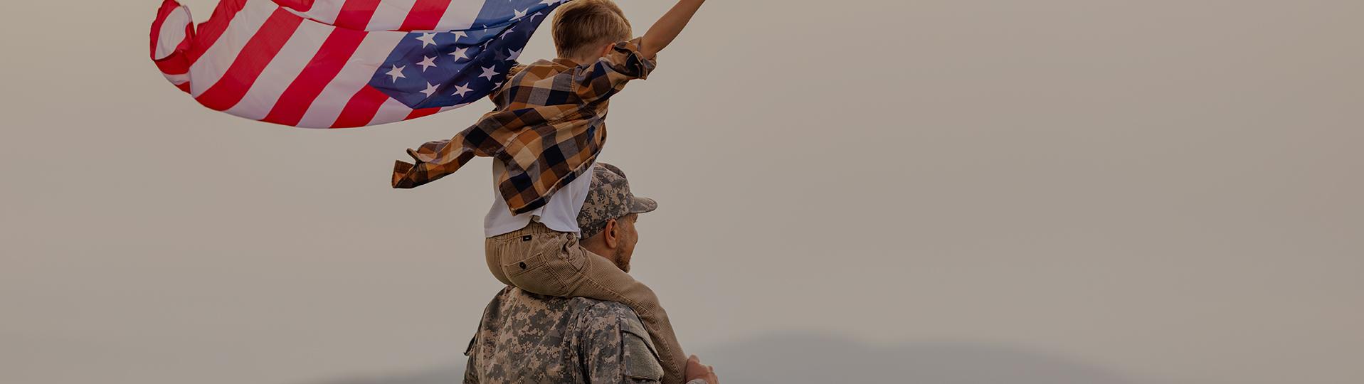 Un soldado sostiene orgullosamente a su hijo sobre sus hombros, el niño ondea una bandera estadounidense, lo que simboliza la esperanza del parole in place militar para su familia.